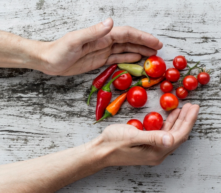 A person's open hands around a collection of small peppers and tomatoes against a rustic white table. 